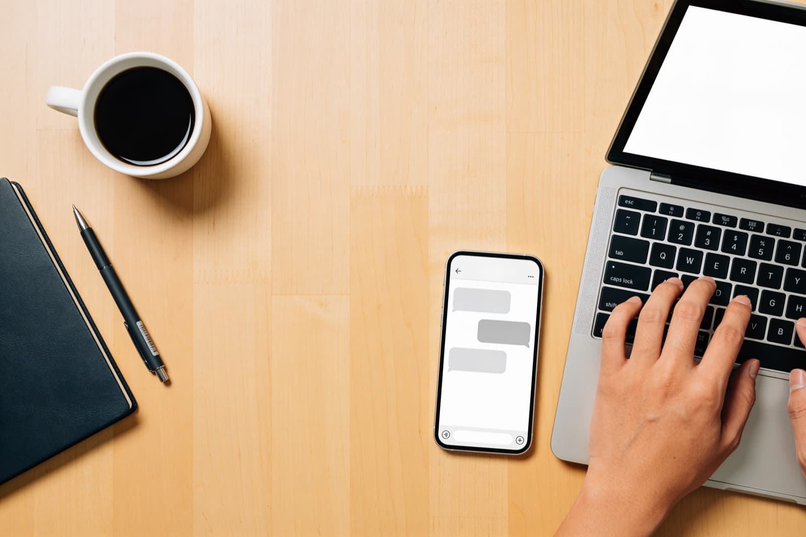 Schreibtisch von oben mit Laptop und Smartphone, auf dem eine Chat-Oberfläche zu sehen ist