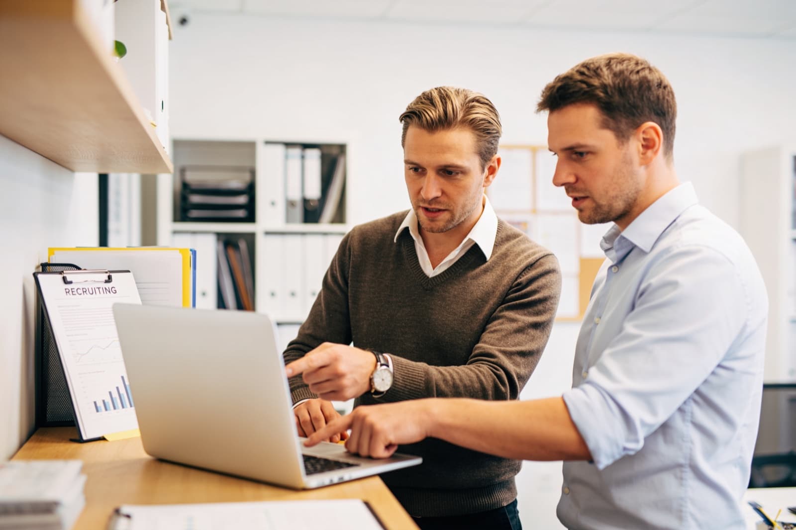 Agenturinhaber und Kollege besprechen einen automatisierten Workflow am Laptop