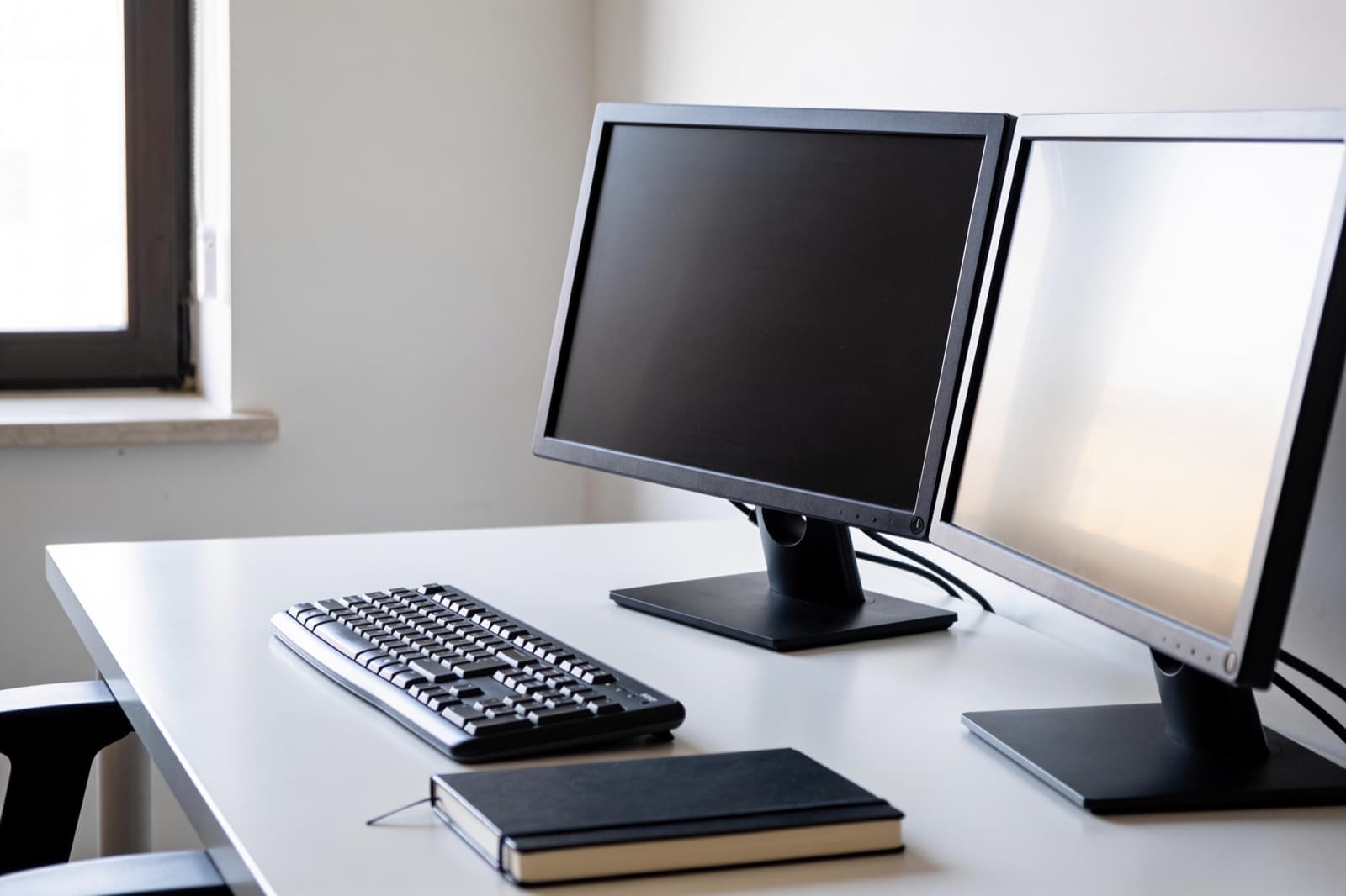 Schreibtisch mit zwei Bildschirmen und Tastatur in einem hellen Büro